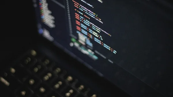 Computer screen displaying lit programming code over a dark keyboard.