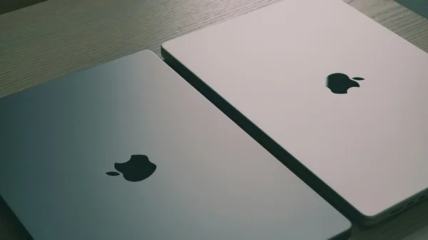 Two closed MacBooks side by side on a wooden table.