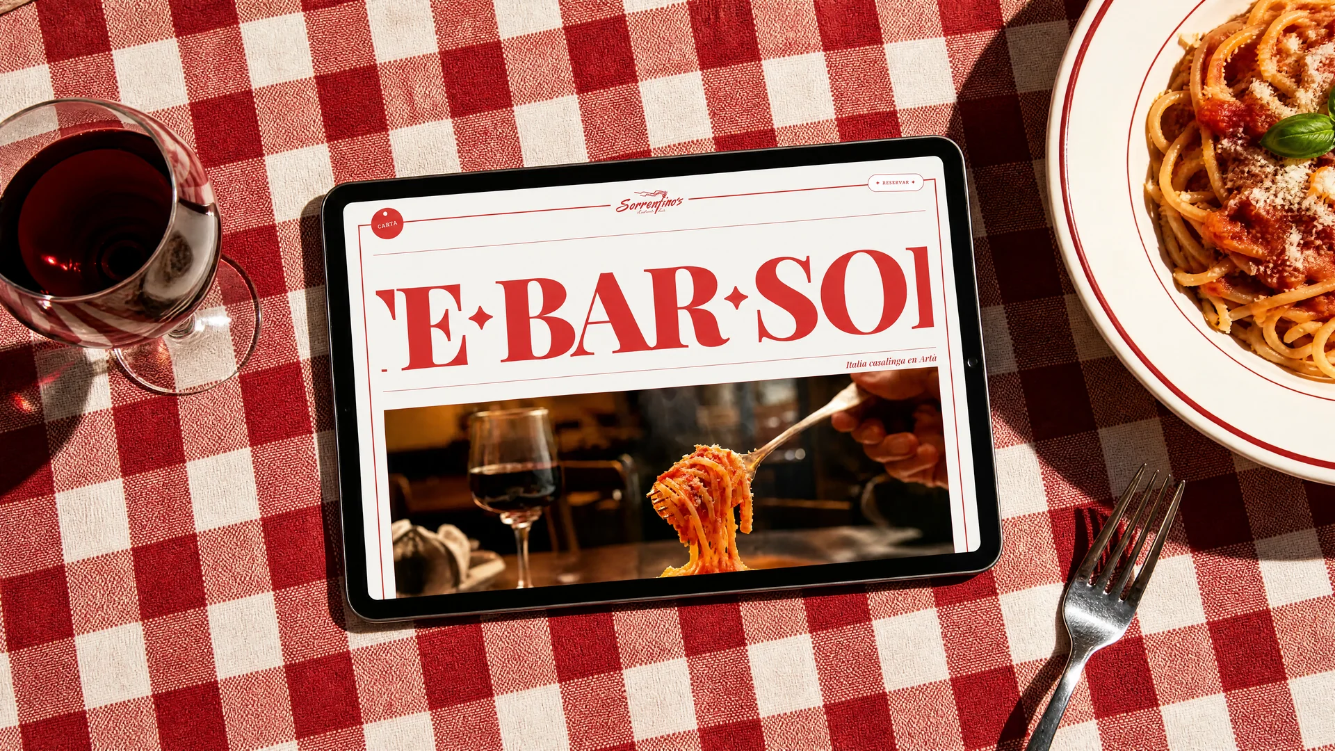 La web de Sorrentino's en una tablet sobre el mantel de cuadros rojos de la trattoria, junto a un plato de pasta y una copa de vino